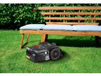 Robotic lawnmower on green grass in front of a wooden garden bench with light blue cushions.