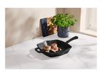 Grilled meat with vegetables in a black griddle pan on a white marble surface.
