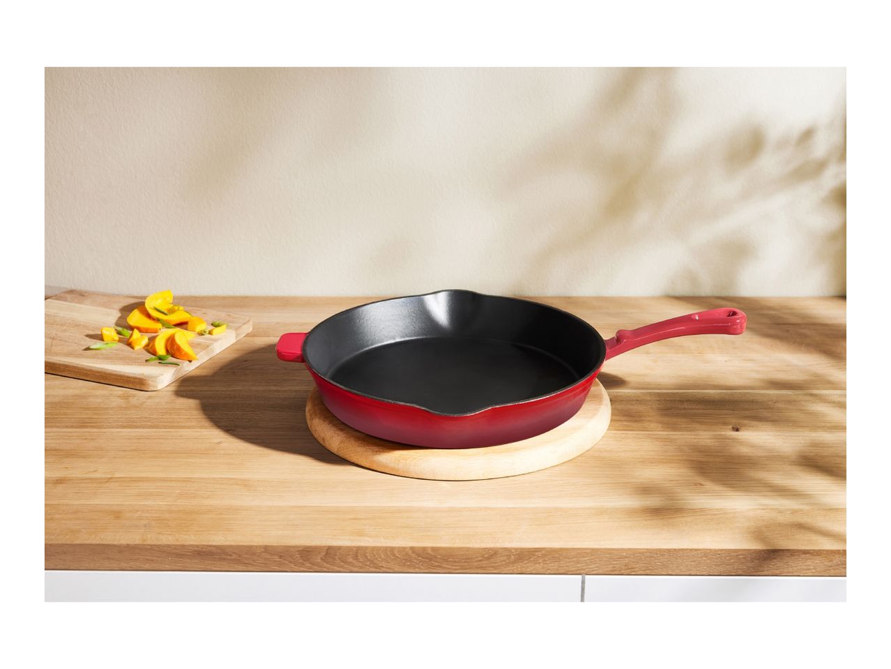 Red cast iron skillet on a wooden cutting board with chopped vegetables.