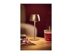 A modern table lamp illuminates a wooden table with a drink and a magazine.