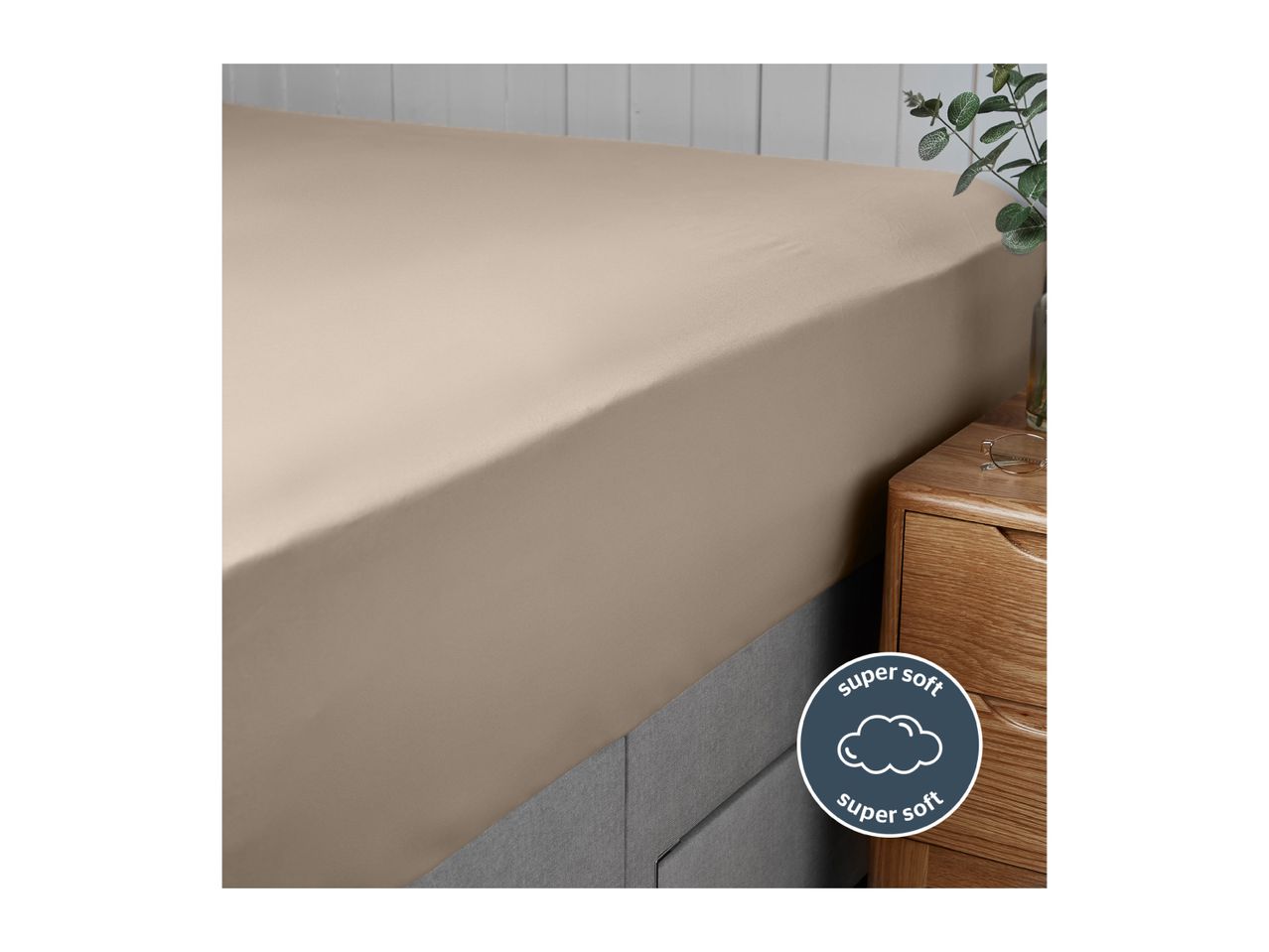 A close-up of a beige fitted bed sheet on a bed, with a 'super soft' label.