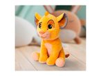 A plush toy of a young lion cub, sitting on a wooden floor with blurred toys in the background.