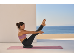 Woman in activewear doing pilates on a mat with a balance cushion, overlooking the sea.