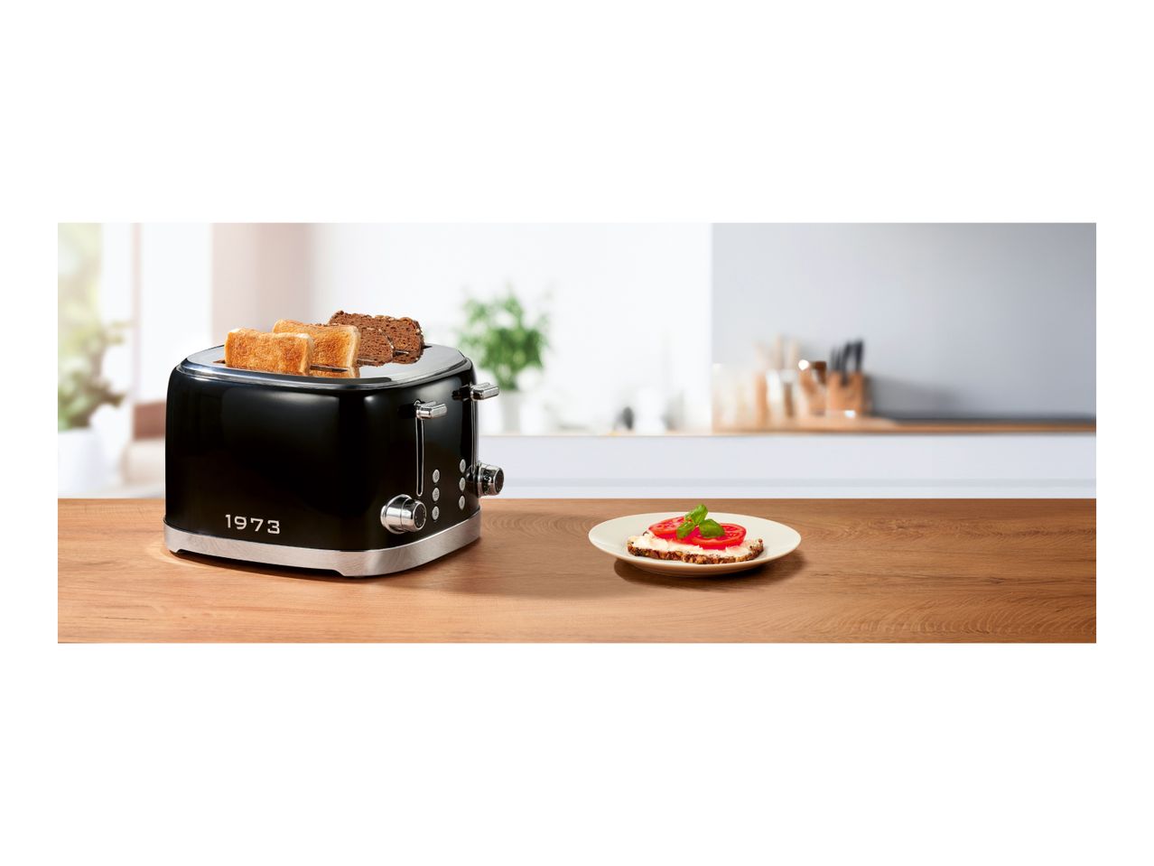Black retro 4-slice toaster with '1973' text on a wooden kitchen counter next to a plate.