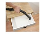 A person vacuums dirt out of a wooden drawer using a black vacuum cleaner attachment.