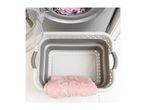 A collapsible laundry basket sits next to a washing machine, containing a pink towel.