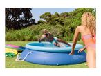 Man jumping into an inflatable pool with a ball, woman watching in a sunny garden.