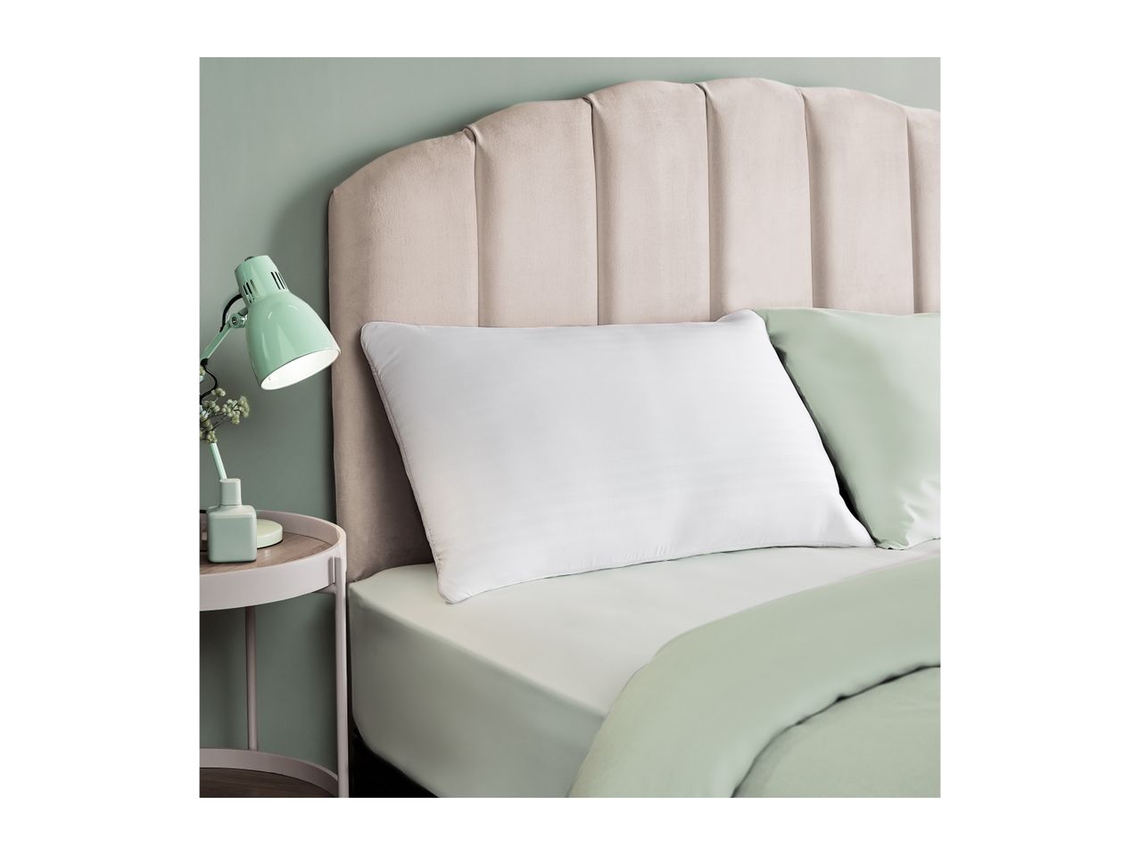 A bed with a beige headboard, white pillow, and light green bedding, next to a mint green lamp.