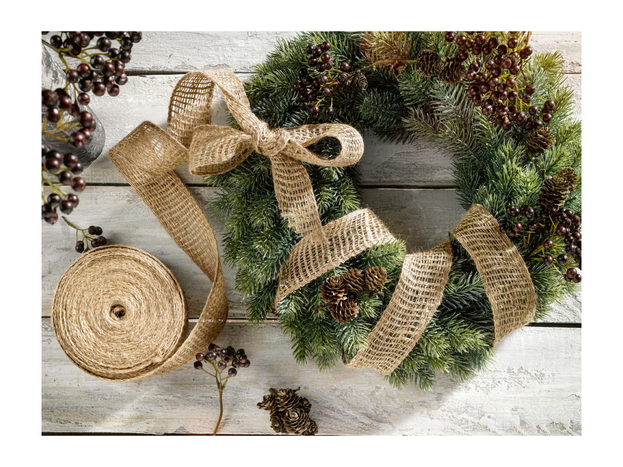 A green Christmas wreath decorated with pine cones, berries, and a burlap ribbon.