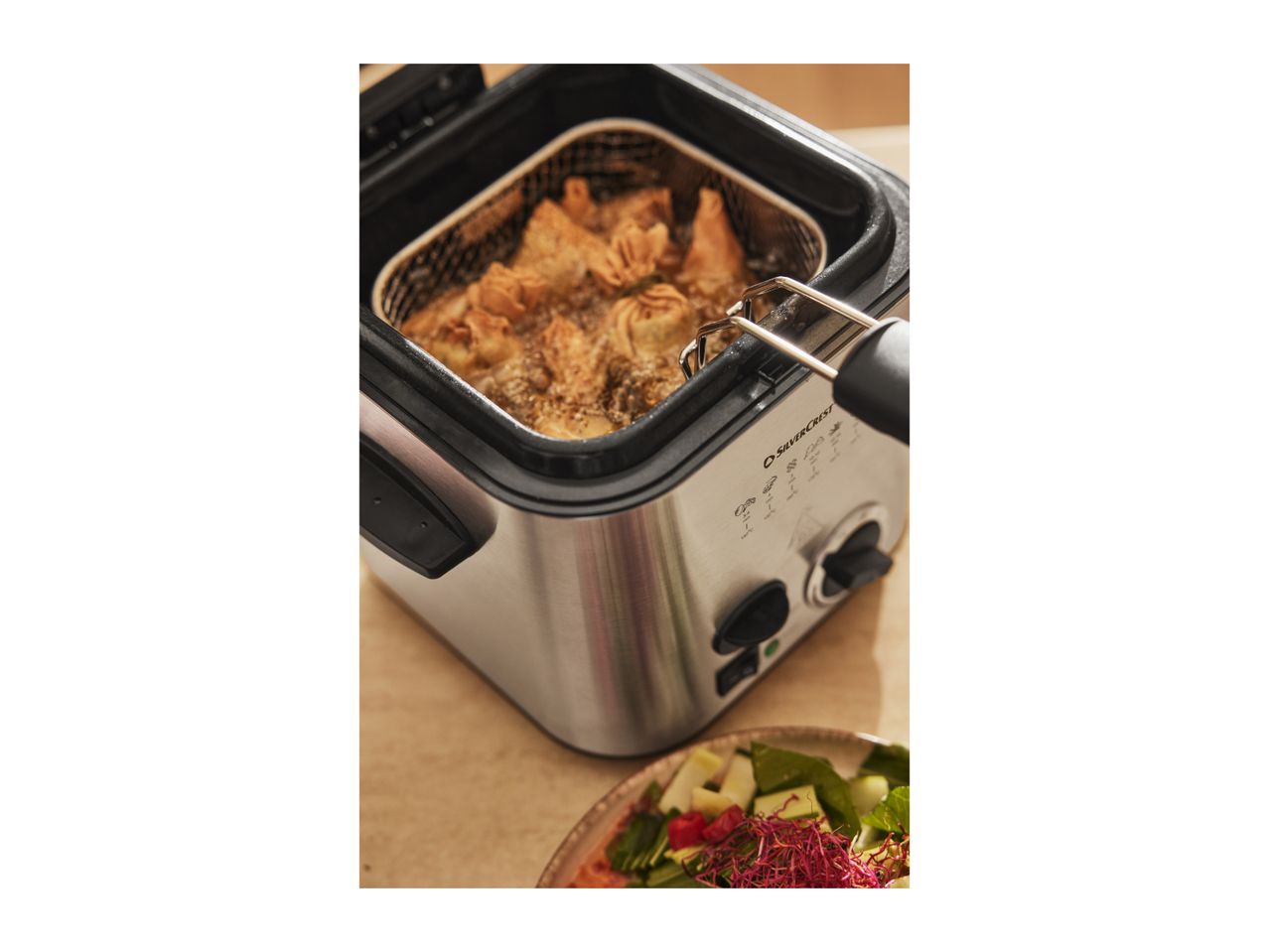 SilverCrest deep fryer with food frying inside, next to a fresh salad.