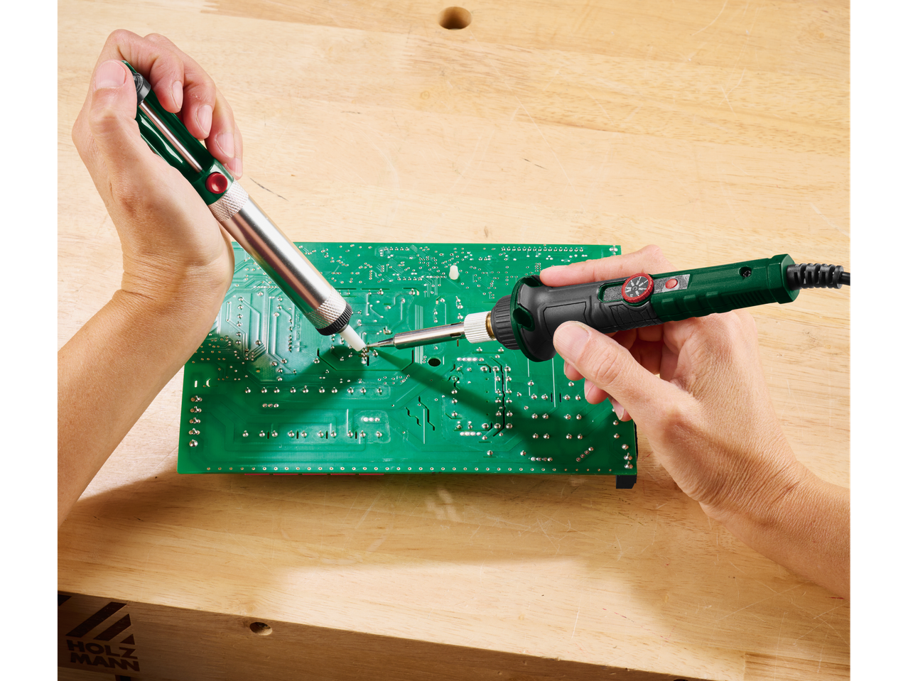 Ένα άτομο αποκολλά μια πλακέτα κυκλώματος με κολλητήρι και αντλία αποκόλλησης.