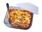 A glass baking dish with a frittata, a serving spoon, and a white plastic lid.
