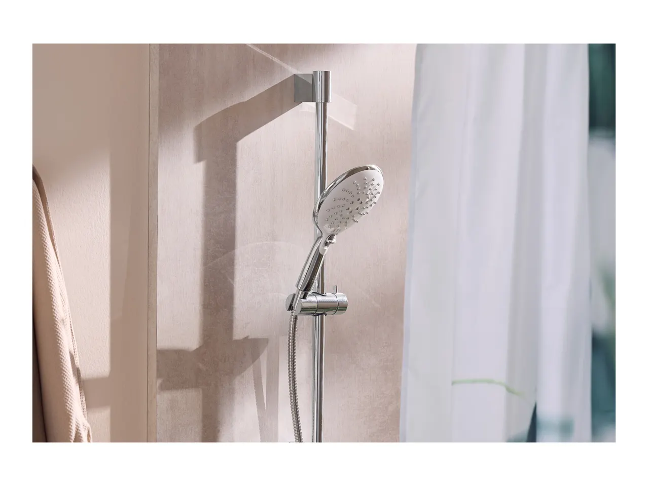 Chrome shower head and rail in a modern bathroom with a white shower curtain.