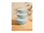 Stack of three light green mixing bowls with white lids on a wooden surface.