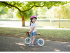 Girl in pink helmet riding a balance bike in a park.