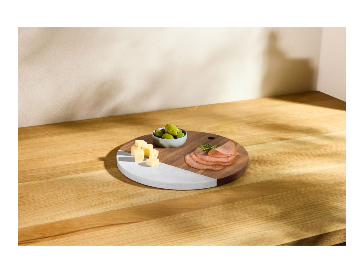 Round serving board with cheese cubes, olives, and sliced meat on a wooden surface.