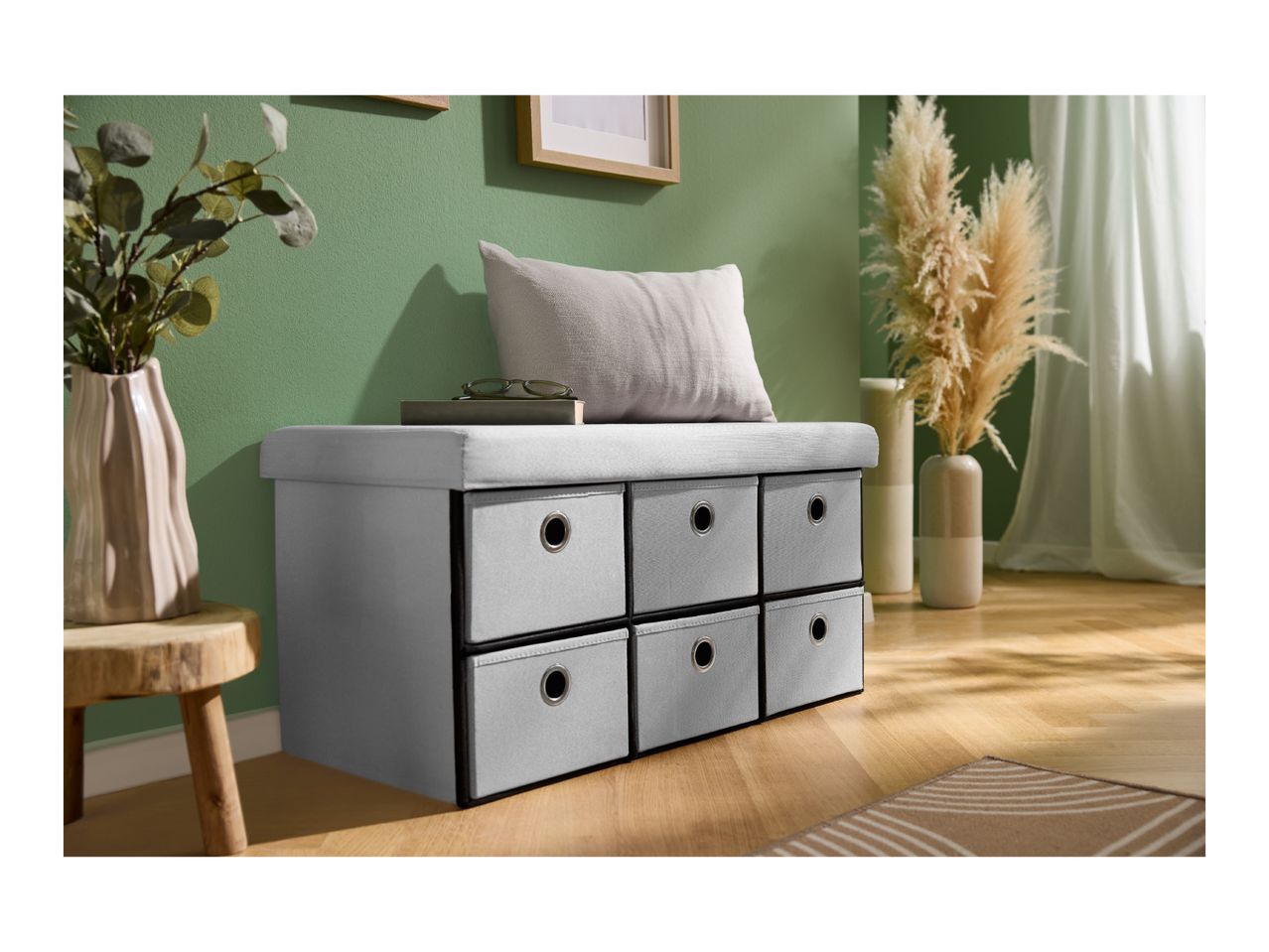Grey storage bench with six fabric drawers, a cushion, and decorative plants in a room.