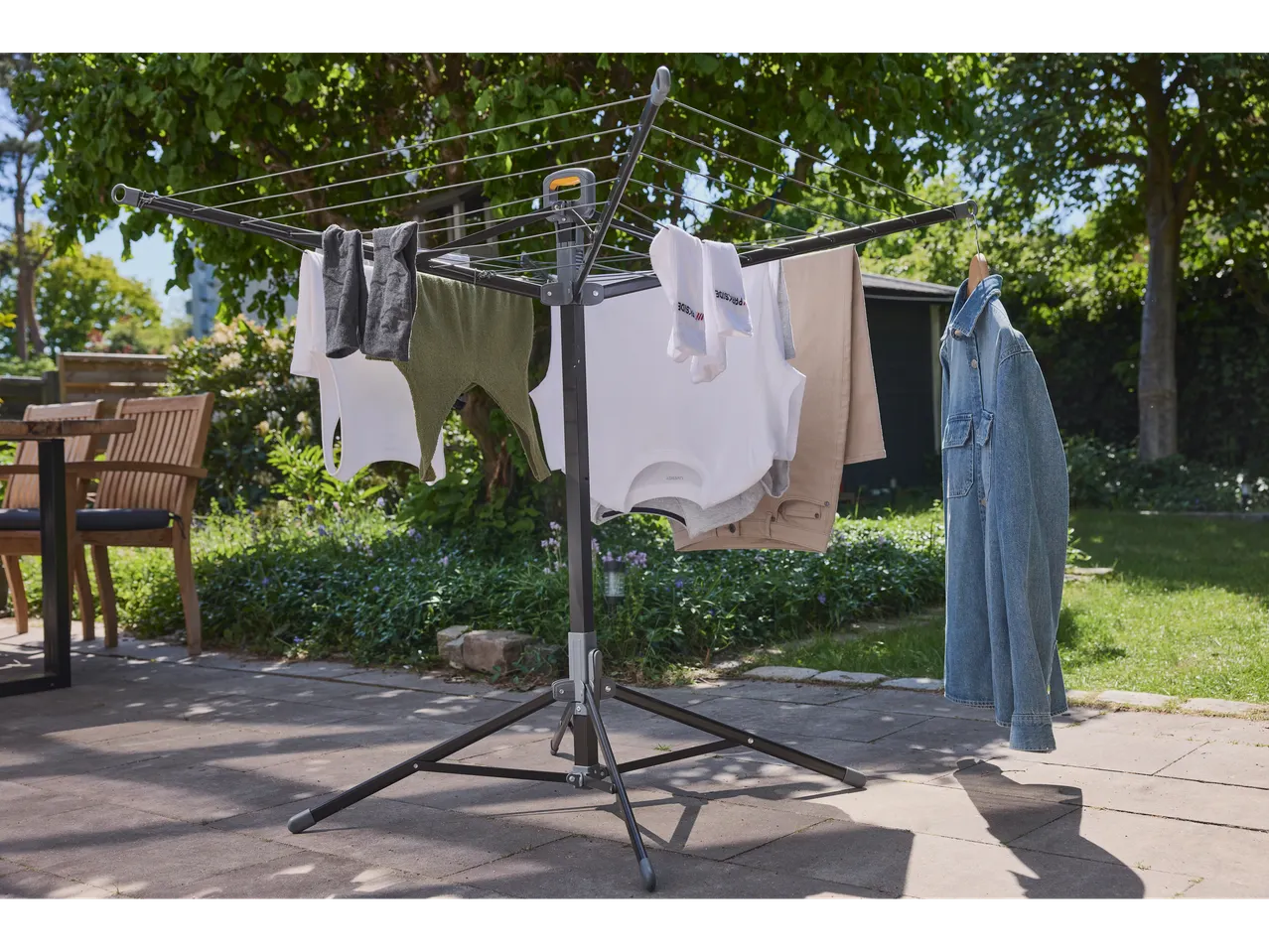 A Brabantia rotary clothes airer stands in a sunny garden, drying various clothing items.