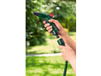 Hands connecting a green garden hose nozzle to a coiled hose in a garden.