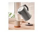 A gray SilverCrest electric kettle pouring hot water into a mug on a wooden counter.