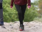 A person in black leggings and a maroon jacket walking on a dirt path.