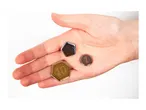 A hand holding three game tokens: a gold 10, a silver 5, and a bronze 1.