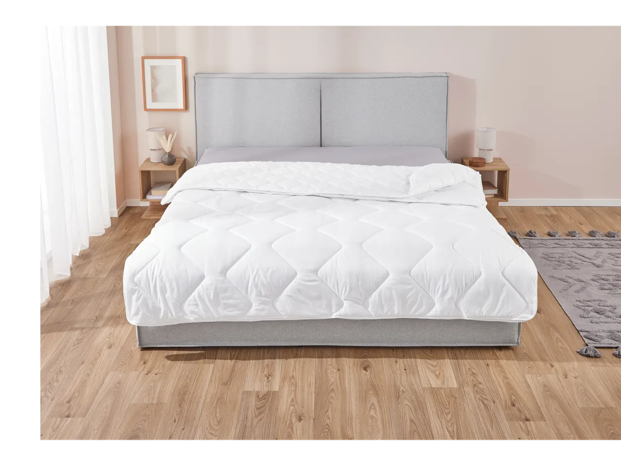 A modern bedroom with a grey upholstered bed, white duvet, and wooden nightstands.