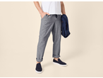 Homem de calças cinzentas, t-shirt branca e mocassins azul-escuros, com um casaco ao braço.