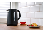 Black SILVERCREST® electric kettle with a cup of tea and a cake on a wooden countertop.