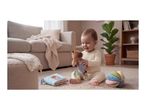 Happy baby playing with a soft toy, fabric book, and sensory ball on a rug.