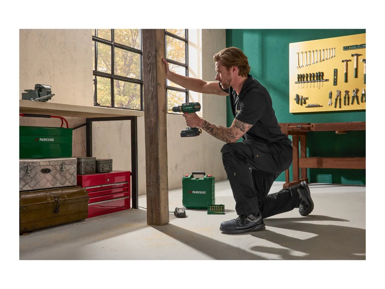 Man using a cordless drill to work on a wooden beam in a workshop setting.