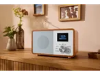 TRONIC® radio na drvenoj komodi, sa vazama i slikama u pozadini.