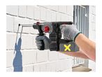 A person drilling into a white brick wall with a cordless rotary hammer drill.