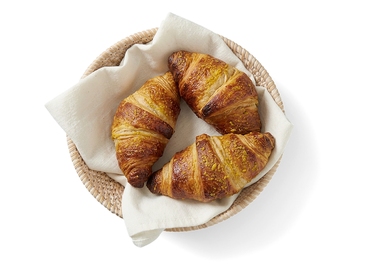 Drie goudbruine croissants met pistachekruimels in een rieten mandje met een wit servet.