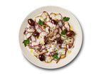 Octopus carpaccio with olives, parsley, and lemon zest, drizzled with olive oil on a white plate.