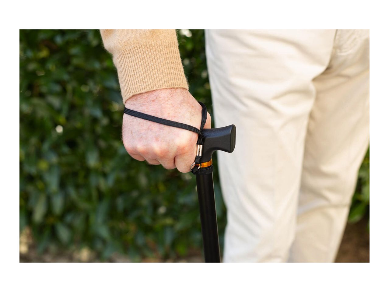 Close-up of an elderly person's hand holding a walking stick with a wrist strap.
