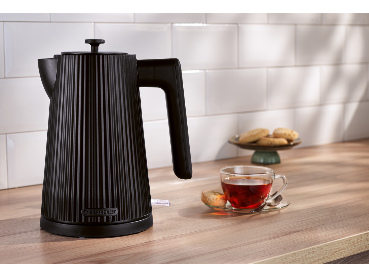 SILVERCREST® 3000W Kettle in black, with tea and cookies on a wooden counter.
