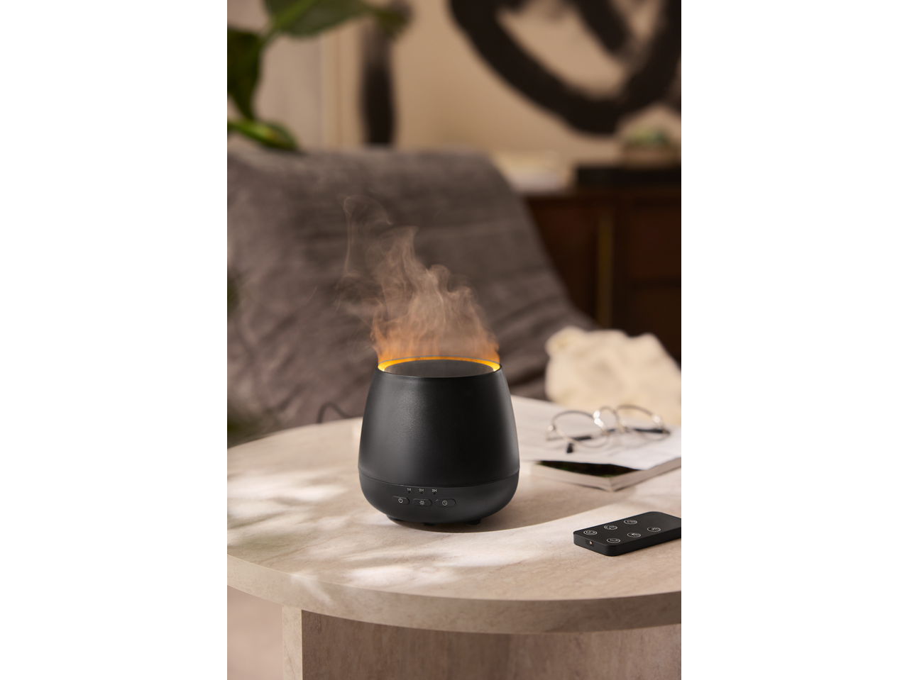 Black aroma diffuser with flame effect and remote control on a side table.
