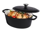 Black oval cast iron casserole dish with lid, filled with roasted chicken, tomatoes, and vegetables.