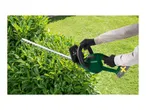 A person wearing gloves trims a green hedge with a hedge trimmer.