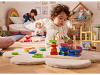 Toddlers playing with wooden stacking toys on a rug in a bedroom.