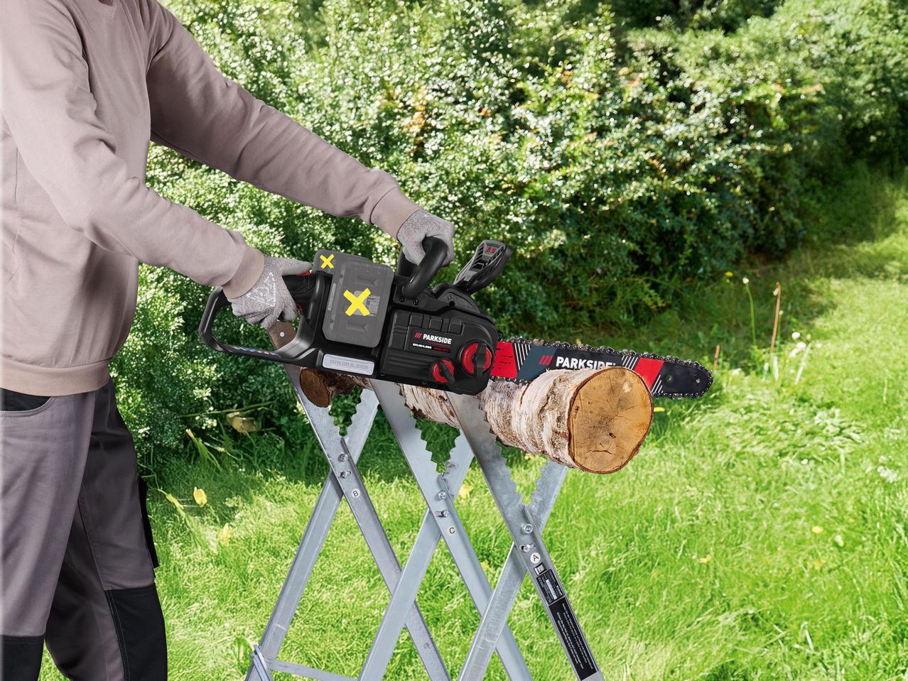 Férfi vág fát egy fűrészbakon akkumulátoros láncfűrésszel.