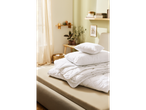 A neatly folded white duvet and pillows sit on a beige bed in a minimalist bedroom.
