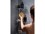 A person showering, holding a natural sponge, with shower caddy and bottles.