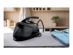 A black steam generator iron on an ironing board next to a folded blue polo shirt.