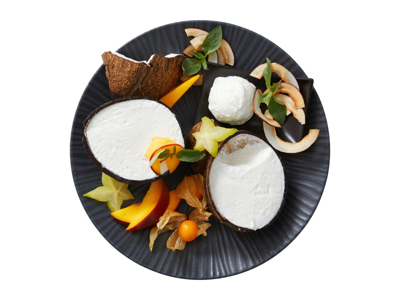 Coconut dessert with fresh fruit, coconut flakes, and mint on a dark plate.