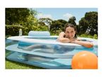 Woman relaxing in an inflatable pool in a garden with an orange ball.