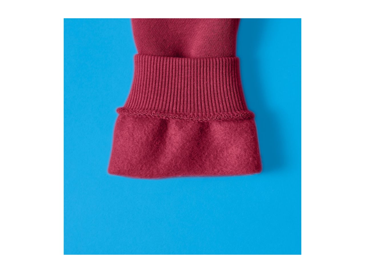 Close-up of a burgundy sweatshirt cuff with ribbed knit and fleece lining.