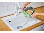Escorrendo macarrão com um escorredor de silicone verde na pia da cozinha.