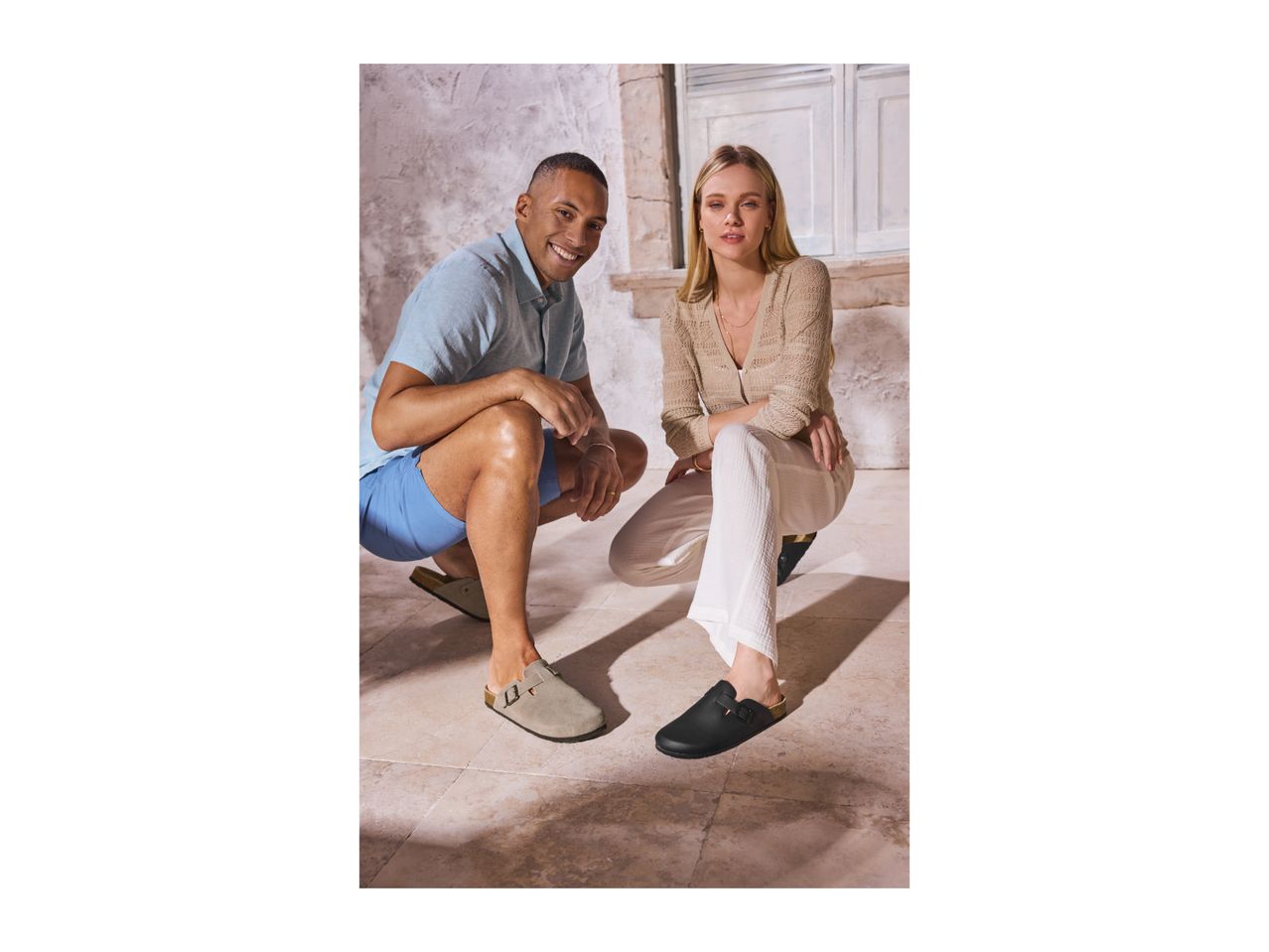 Two people in casual wear, wearing clogs, crouching on a tiled floor.